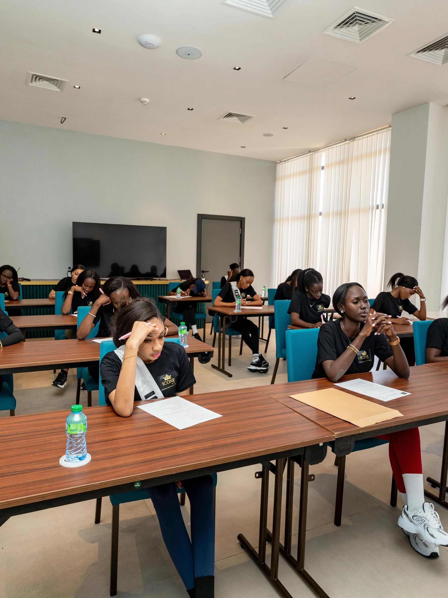 La salle d’examen : les candidates réparties aux tables, penchées sur leur copie